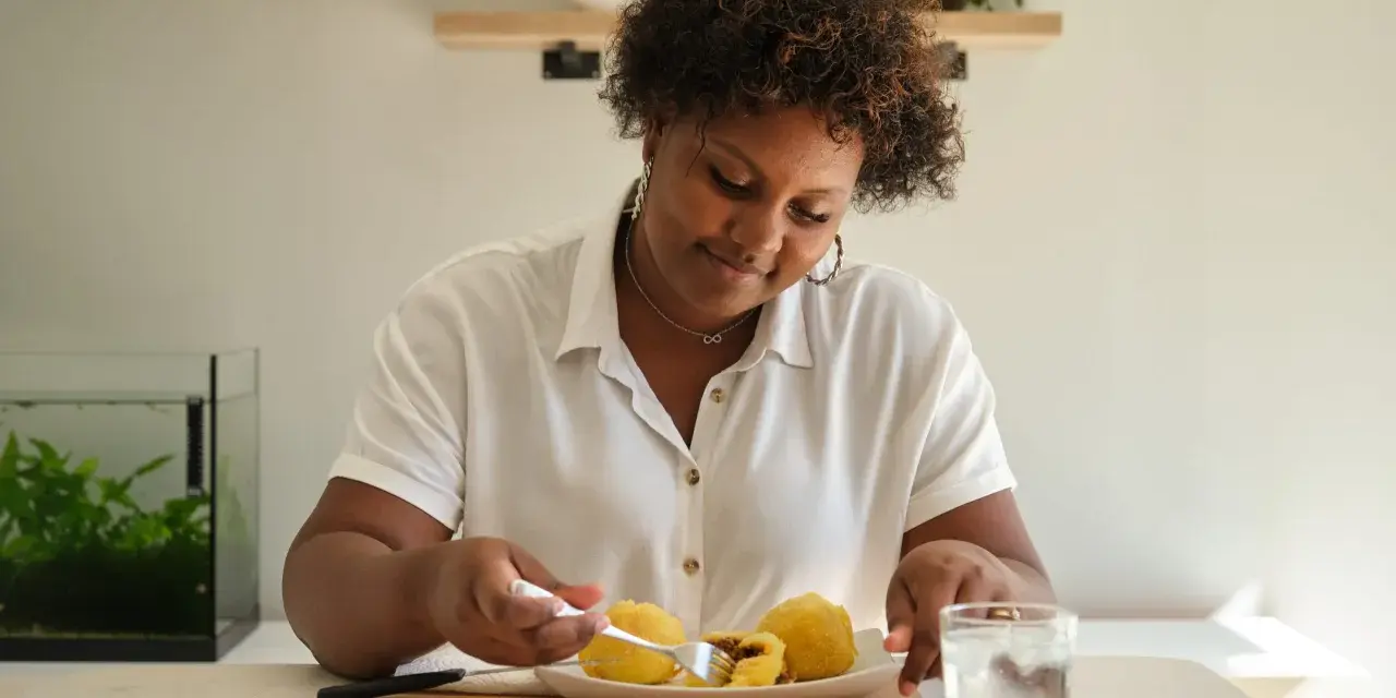 Mujer sonriente disfruta de croquetas de patata, un carbohidrato delicioso, con un vaso de agua.