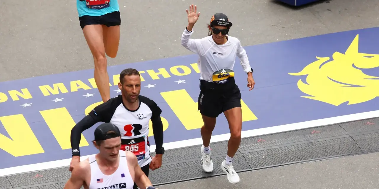 Corredores cruzan la meta en la media maratón de Europa. Una mujer saluda, celebrando su logro.