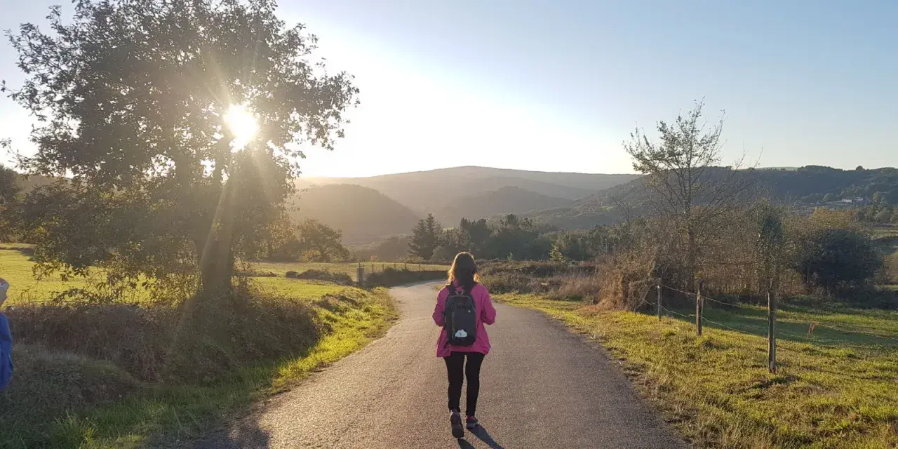 Una peregrina con mochila rosa camina por un sendero rural al atardecer, disfrutando del **camino de Santiago corriendo**.