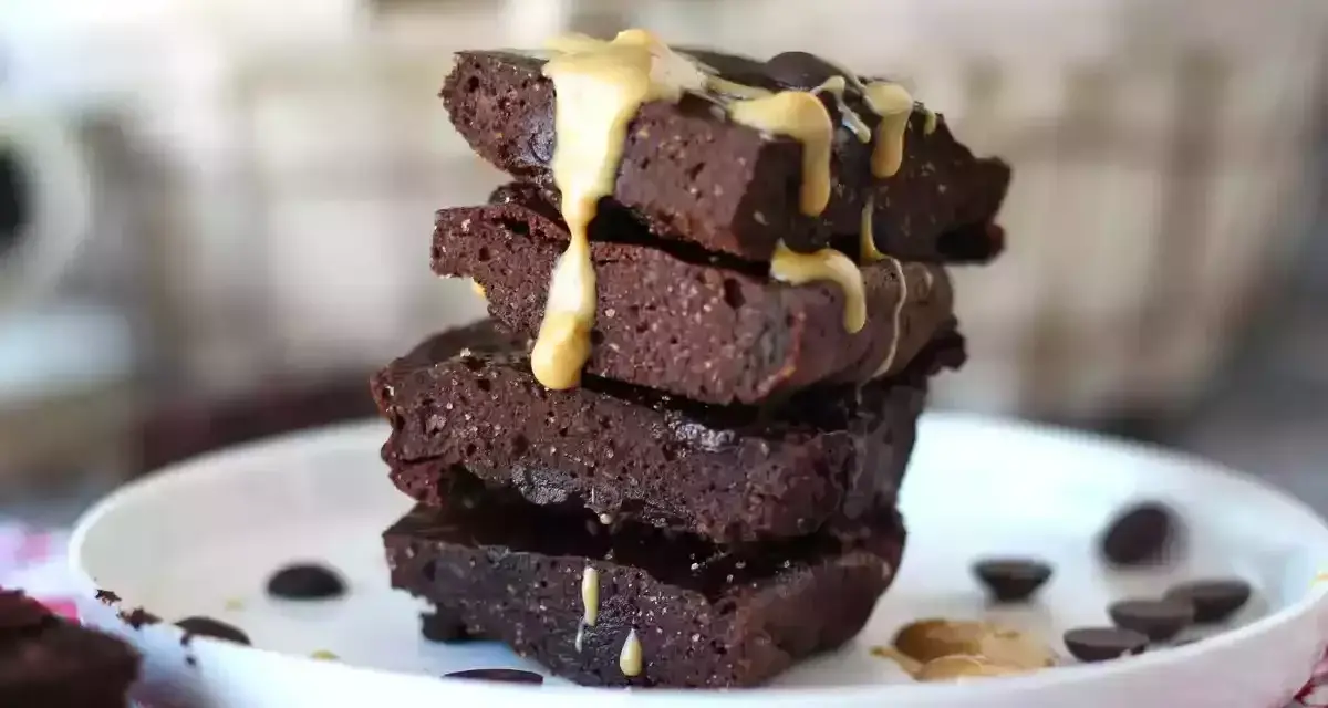 Apilados trozos de brownie de proteína cubiertos con salsa de caramelo y chispas de chocolate.