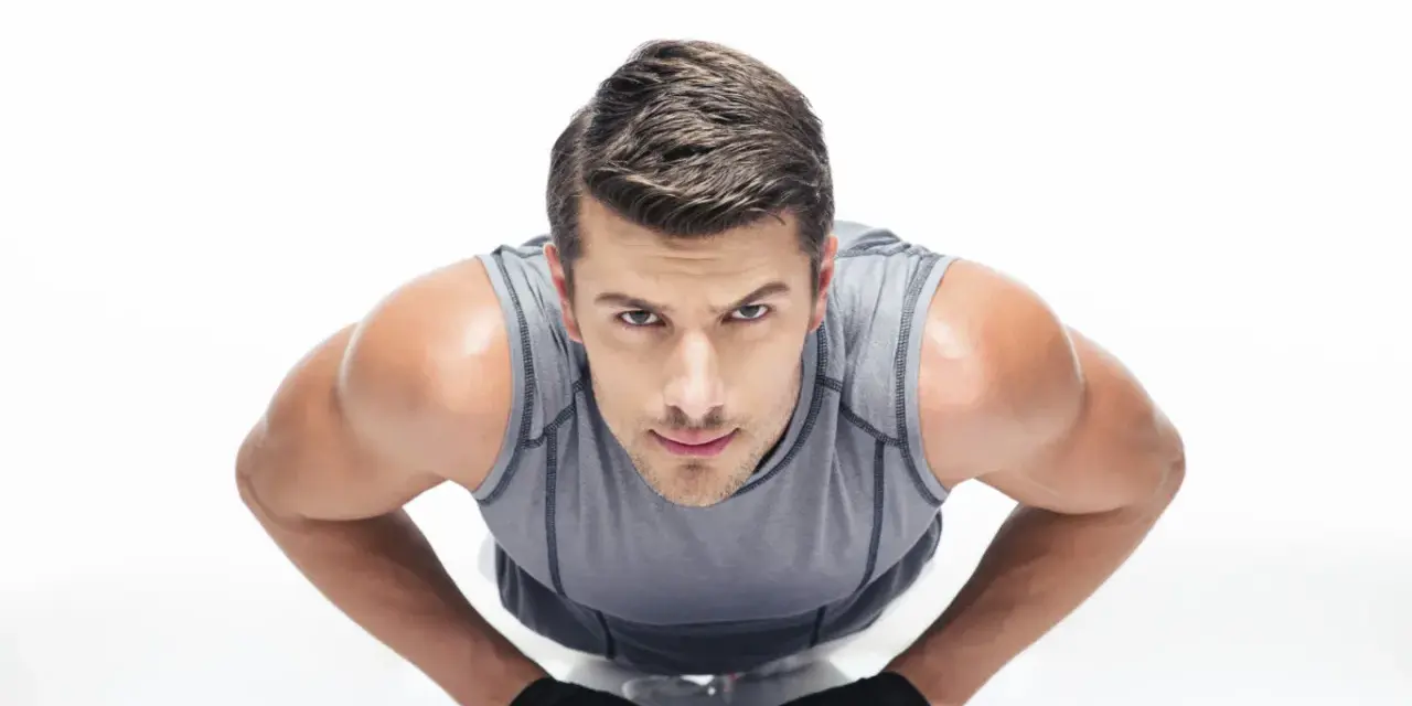 Hombre concentrado haciendo diamond push ups, con guantes negros y camiseta gris.