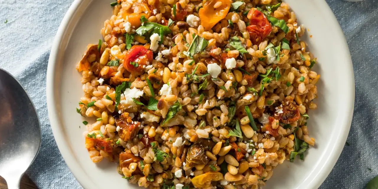 Ensalada de farro que es un plato mediterráneo con tomates secos, piñones y queso feta desmenuzado, todo mezclado con granos de farro.