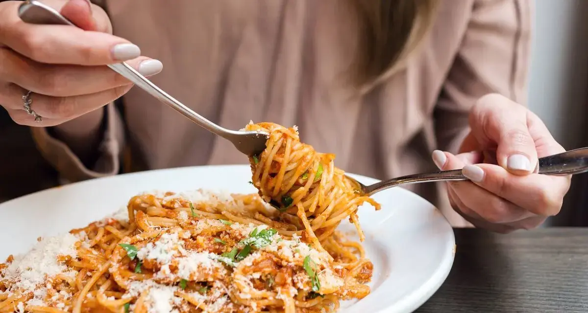 Mujer disfrutando un plato de pasta integral con salsa boloñesa y queso rallado. ¡Cuidado, la pasta integral engorda si no se consume con moderación!