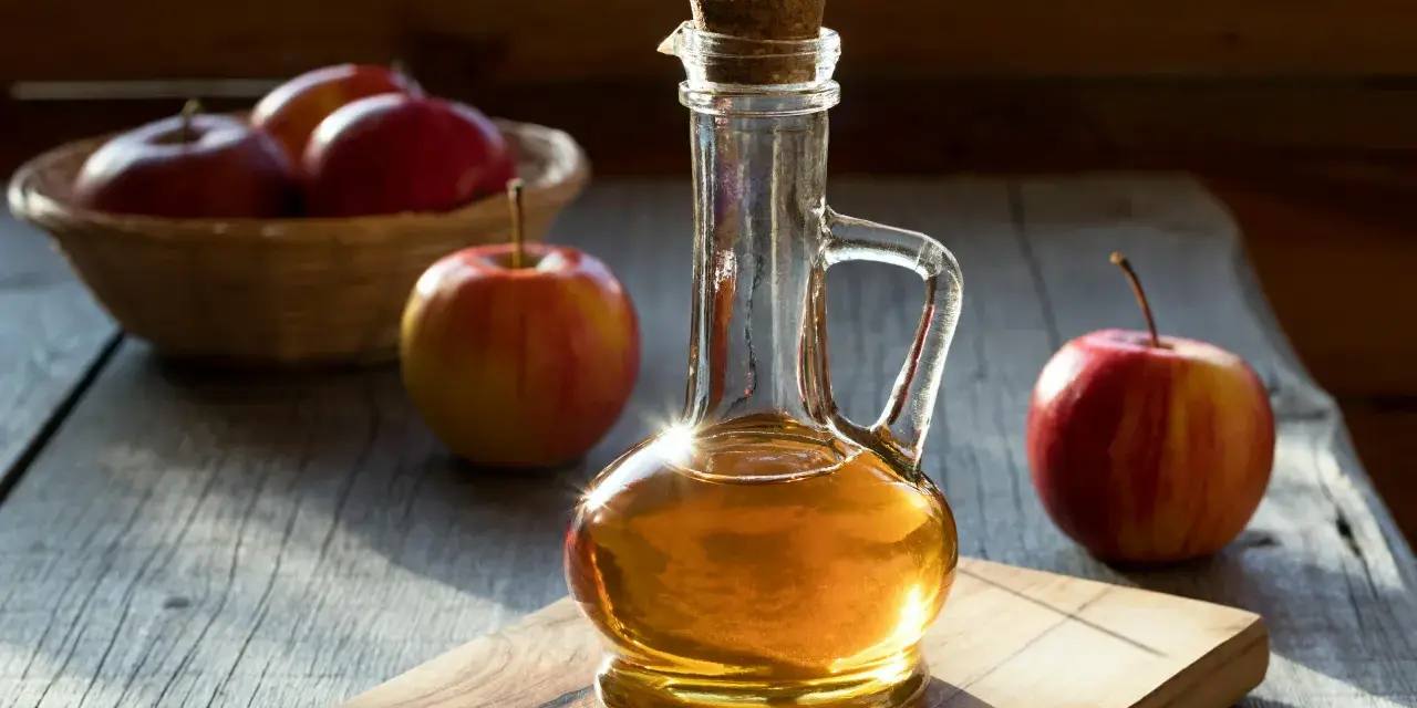 Botella de vinagre de manzana artesanal junto a manzanas rojas. Considera las vinagre de manzana contraindicaciones antes de su uso.