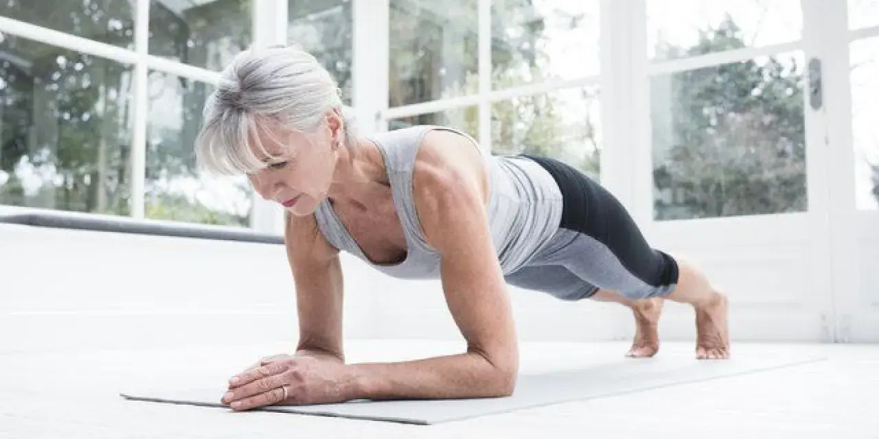 Mujer mayor haciendo plancha en su sala, demostrando que el fitness en casa es para todas las edades.