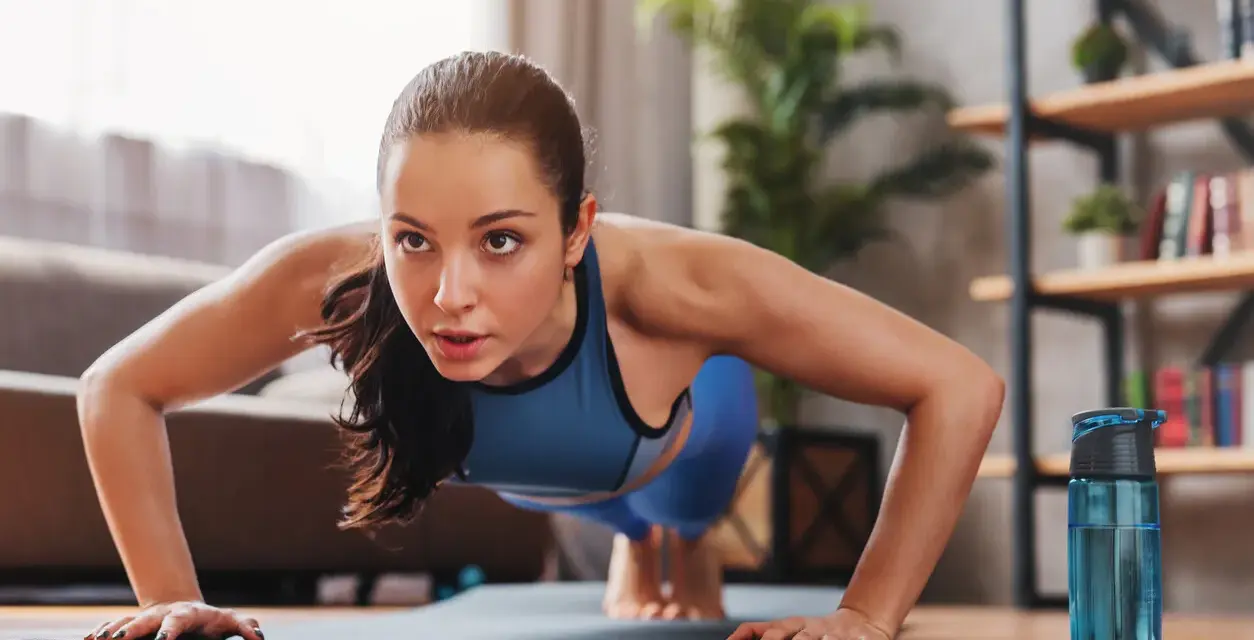 Mujer concentrada haciendo flexiones, parte de sus ejercicios de fuerza en casa.