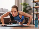 Mujer concentrada haciendo flexiones, parte de sus ejercicios de fuerza en casa.