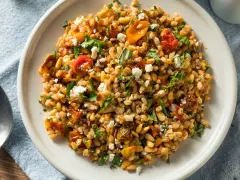 Ensalada de farro que es un plato mediterráneo con tomates secos, piñones y queso feta desmenuzado, todo mezclado con granos de farro.