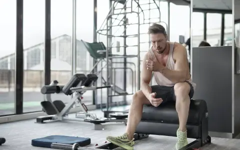 Hombre sentado en un banco de gimnasio, reflexionando sobre cuanto descansar entre series.