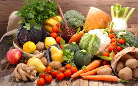 Variedad de tipos de verdura y frutas frescas sobre mesa de madera: brócoli, coliflor, zanahorias, tomates, repollo morado, peras, manzanas, plátanos, limones, jengibre y patatas.