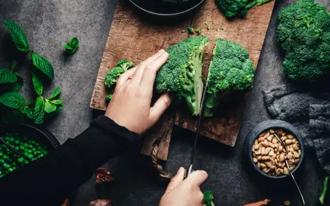 Manos cortando brócoli, un alimento rico en silicio, junto a guisantes y cacahuetes.