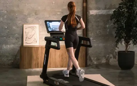 Mujer pelirroja corre en cinta, entrenando en casa con estilo.