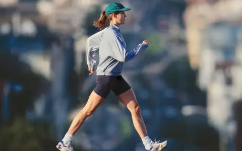 Mujer con gorra y sudadera gris corriendo al aire libre, disfrutando de un paseo después de comer para mantenerse activa.