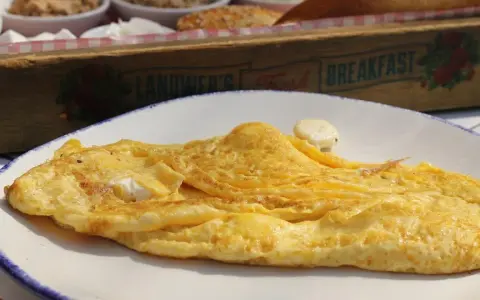 Tortilla francesa dorada en plato blanco, con un toque de queso. ¡Cuidado, la tortilla francesa engorda si no la acompañas con ensalada!