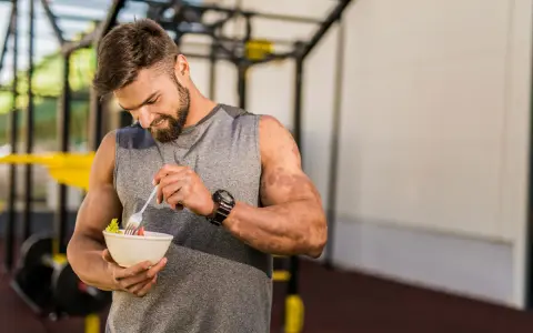 Hombre con barba en gimnasio, comiendo ensalada. Demuestra que se puede ganar músculo en déficit calórico con la dieta adecuada.