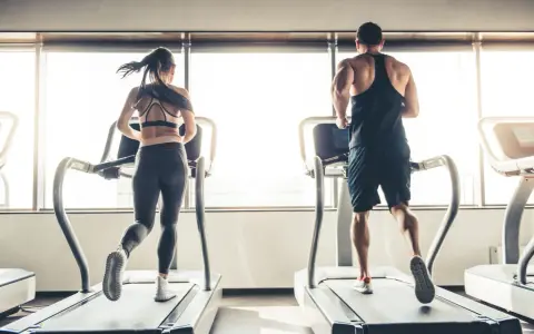 Hombre y mujer corriendo en cintas de correr, disfrutando de su rutina de cardio en ayunas.