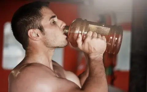 Hombre bebiendo de una botella grande, preparándose para el entrenamiento. ¿Cuántos gramos de pre entreno tomar?