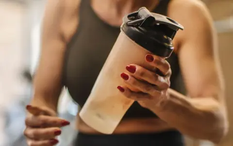 Mujer con uñas rojas sostiene un batido. ¿Los BCAA engordan? La respuesta depende de tu dieta.