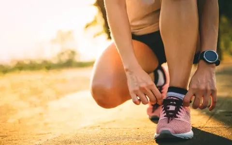 Persona se agacha para atarse los cordones de sus zapatillas rosas, lista para salir a correr al amanecer.