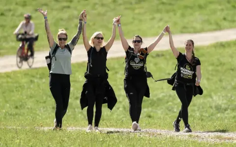 Cuatro mujeres celebran tomadas de la mano, con los brazos en alto, mientras caminan por un sendero. Su **velocidad media andando** parece alegre y enérgica.