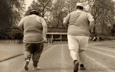 Dos personas con sobrepeso corren en una pista de atletismo. El andar adelgaza, y ellos lo saben.