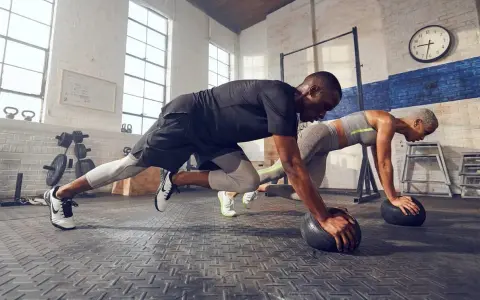 Pareja haciendo cardio en casa, en posición de plancha con balones medicinales.