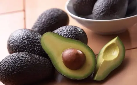 Aguacates frescos, uno cortado por la mitad mostrando su semilla, perfectos para comer aguacate todos los días y disfrutar de su cremosidad.