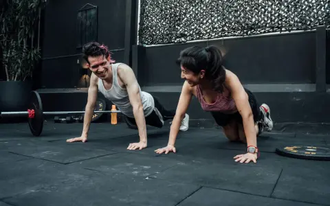 Pareja sonríe haciendo flexiones, un ejemplo de cuales son los ejercicios de fuerza.