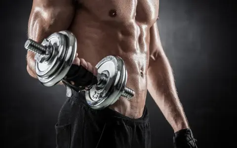 Hombre sudoroso entrenando bíceps con mancuerna. Descubre cuántas repeticiones hacer para ganar masa muscular y optimizar tu entrenamiento.