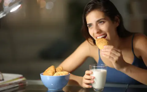 Mujer sonríe mientras come un croissant, pensando en qué picar entre horas que no engorde.