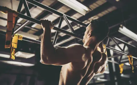 Hombre musculoso realizando pull ups en un gimnasio. Sus brazos y espalda están tensos mientras se eleva.