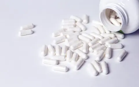 Cápsulas blancas derramadas de un frasco. Descubre para qué sirven los BCAA en mujeres y cómo pueden apoyar tu bienestar.