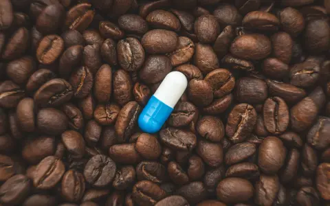 Una pastilla de cafeína azul y blanca descansa sobre granos de café tostados. ¿Cuánto tarda en hacer efecto una pastilla de cafeína?