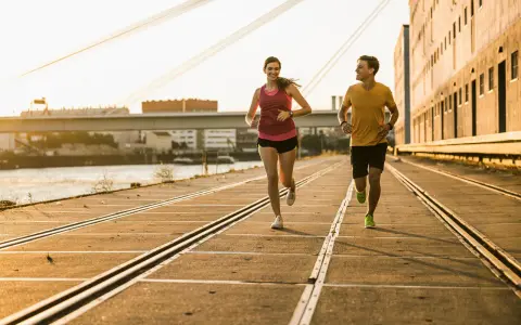 Pareja corriendo al atardecer, demostrando su **endurance crossfit**. El sol dorado ilumina su camino junto al río.