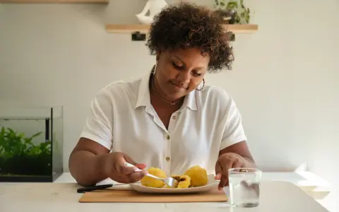 Mujer sonriente disfruta de croquetas de patata, un carbohidrato delicioso, con un vaso de agua.