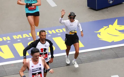 Corredores cruzan la meta en la media maratón de Europa. Una mujer saluda, celebrando su logro.