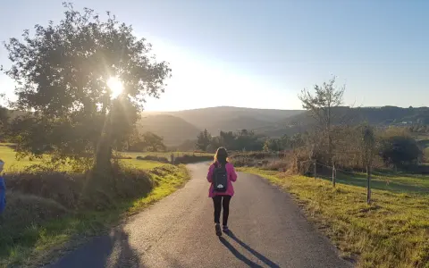Una peregrina con mochila rosa camina por un sendero rural al atardecer, disfrutando del **camino de Santiago corriendo**.