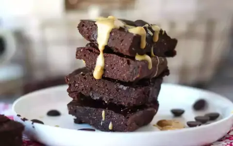 Apilados trozos de brownie de proteína cubiertos con salsa de caramelo y chispas de chocolate.
