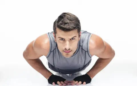 Hombre concentrado haciendo diamond push ups, con guantes negros y camiseta gris.