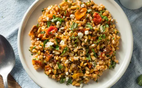 Ensalada de farro que es un plato mediterráneo con tomates secos, piñones y queso feta desmenuzado, todo mezclado con granos de farro.