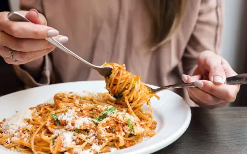 Mujer disfrutando un plato de pasta integral con salsa boloñesa y queso rallado. ¡Cuidado, la pasta integral engorda si no se consume con moderación!