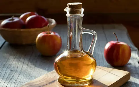 Botella de vinagre de manzana artesanal junto a manzanas rojas. Considera las vinagre de manzana contraindicaciones antes de su uso.
