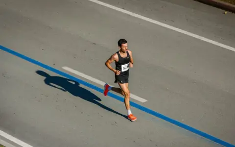 Corredor concentrado en la carrera, aprendiendo como respirar al correr para optimizar su rendimiento. Su sombra se proyecta larga sobre el asfalto.