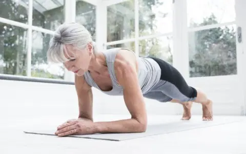 Mujer mayor haciendo plancha en su sala, demostrando que el fitness en casa es para todas las edades.