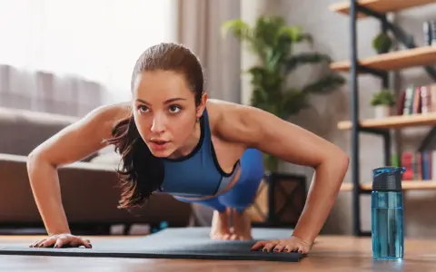 Mujer concentrada haciendo flexiones, parte de sus ejercicios de fuerza en casa.