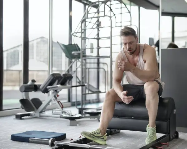 Hombre sentado en un banco de gimnasio, reflexionando sobre cuanto descansar entre series.