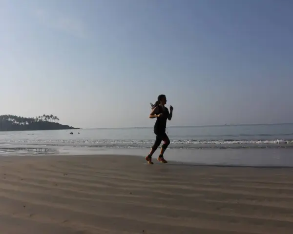 Mujer corriendo en la playa al amanecer, con el mar y una isla con palmeras al fondo.