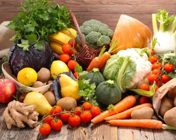 Variedad de tipos de verdura y frutas frescas sobre mesa de madera: brócoli, coliflor, zanahorias, tomates, repollo morado, peras, manzanas, plátanos, limones, jengibre y patatas.