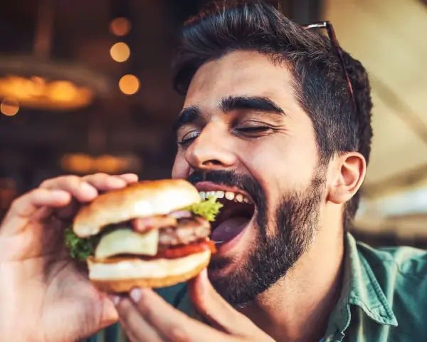 Hombre disfrutando un jugoso **cheat meal** de hamburguesa, con los ojos cerrados por el placer.