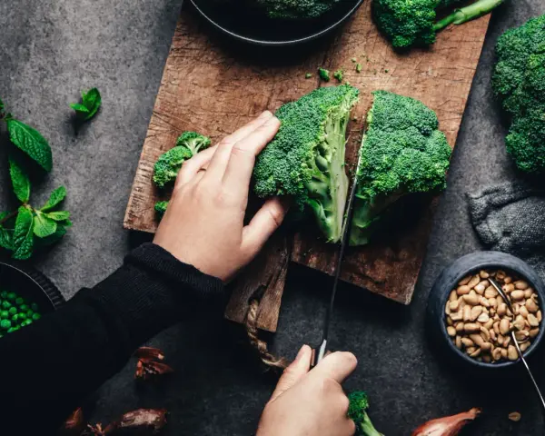Manos cortando brócoli, un alimento rico en silicio, junto a guisantes y cacahuetes.